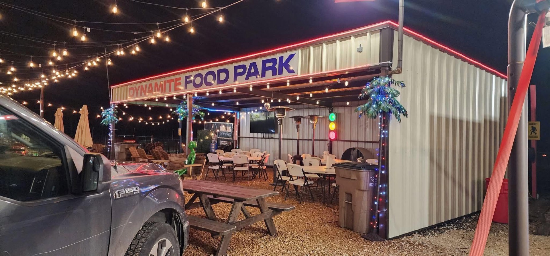 The park at night with the sign lit, string lights on and the pavilion full